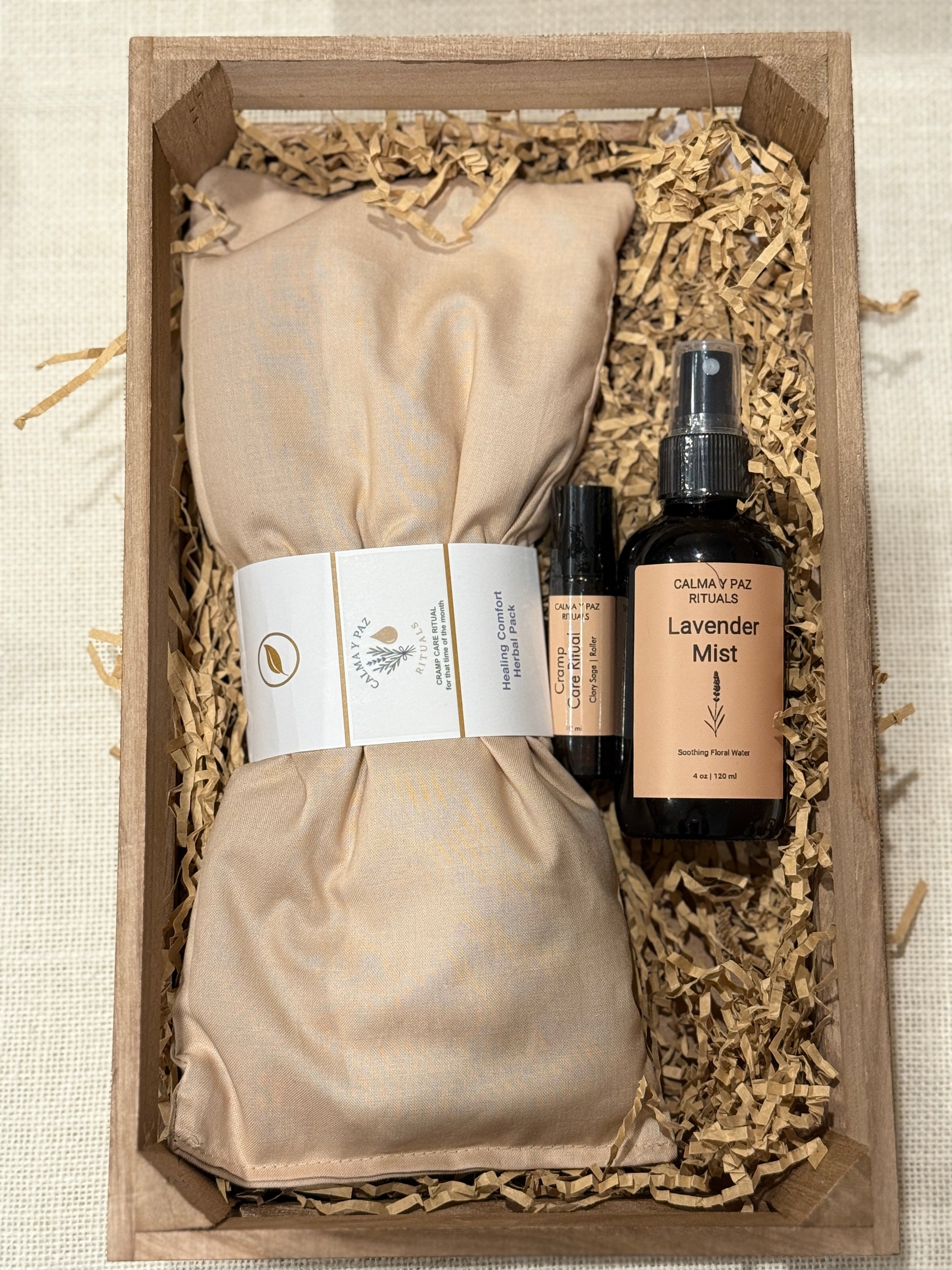 Set of skincare products including a bottle and sprays in a wooden box with natural fibers. Calma y paz rituals Cramp care kit.